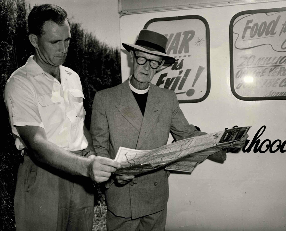 This is a photo of Neville Brooke and Father Tucker on the Food for Peace campaign trail. They are standing together looking at a large document.