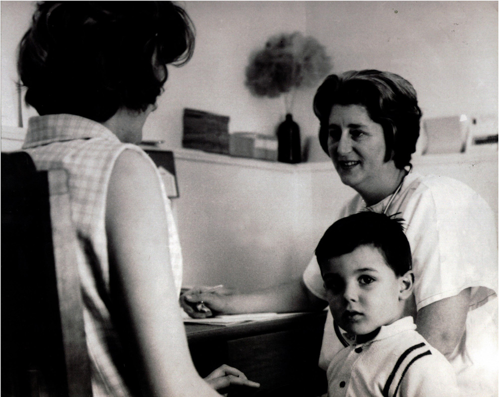 This is a black and white photograph of a mother and her young son talking to staff at the Family Planning Clinic