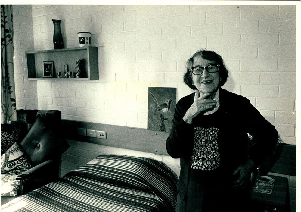 A photo of a resident in her room at Sambell lodge an aged care facility. She is smiling at the camera.