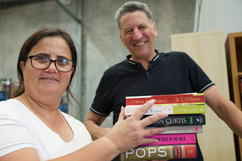 This is a photo of two volunteers sorting books for Brotherhood Books at the warehouse. They are both smiling and happy.